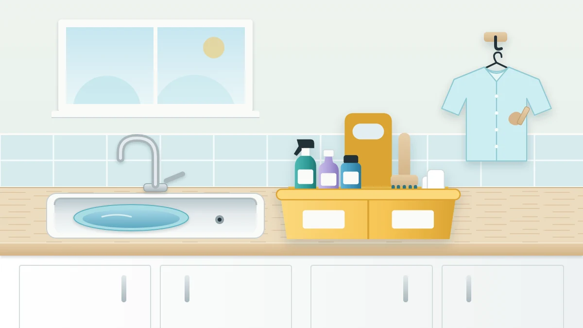 Utility sink in a wooden counter with a handled caddy of bottles, a brush and white cloths, and a shirt hanging on a wall hook